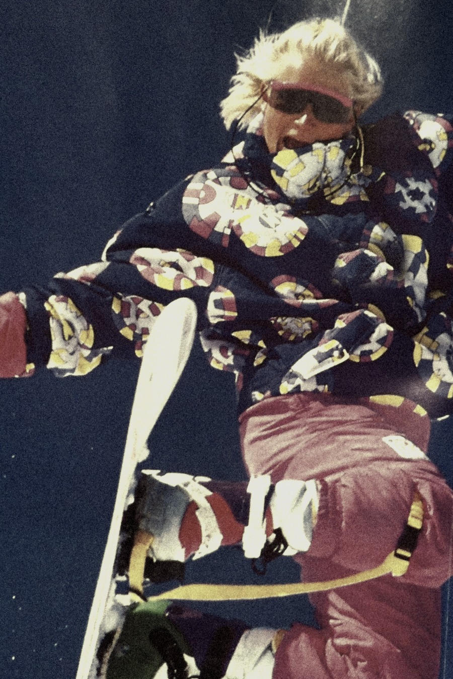 1990s snowboarder in a patterned Chiemsee suit jumping against a deep blue sky